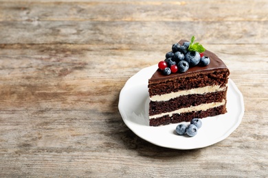 Photo of Plate with slice of chocolate sponge berry cake on wooden background