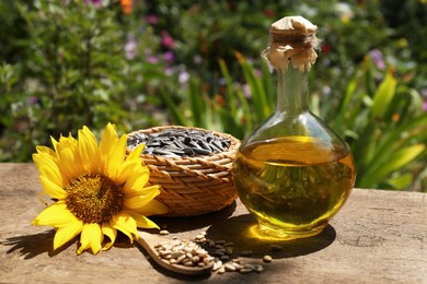 Bottle of sunflower oil, seeds and flower on wooden table outdoors