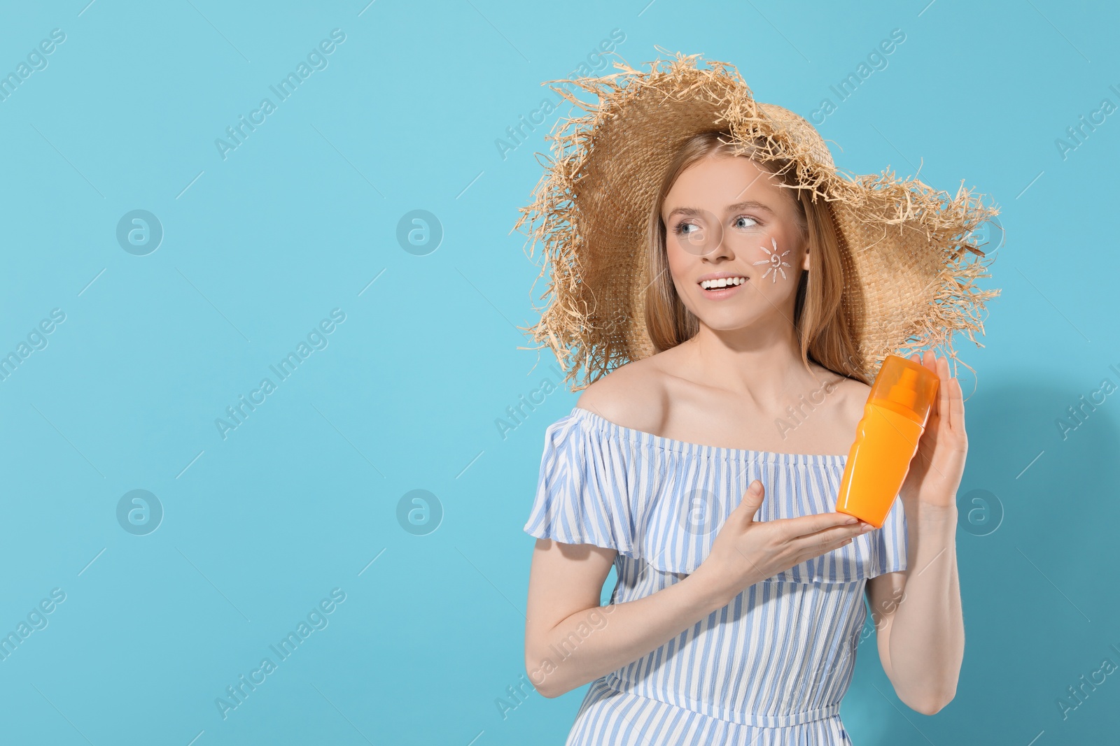 Photo of Beautiful young woman in straw hat with sun protection cream on light blue background, space for text