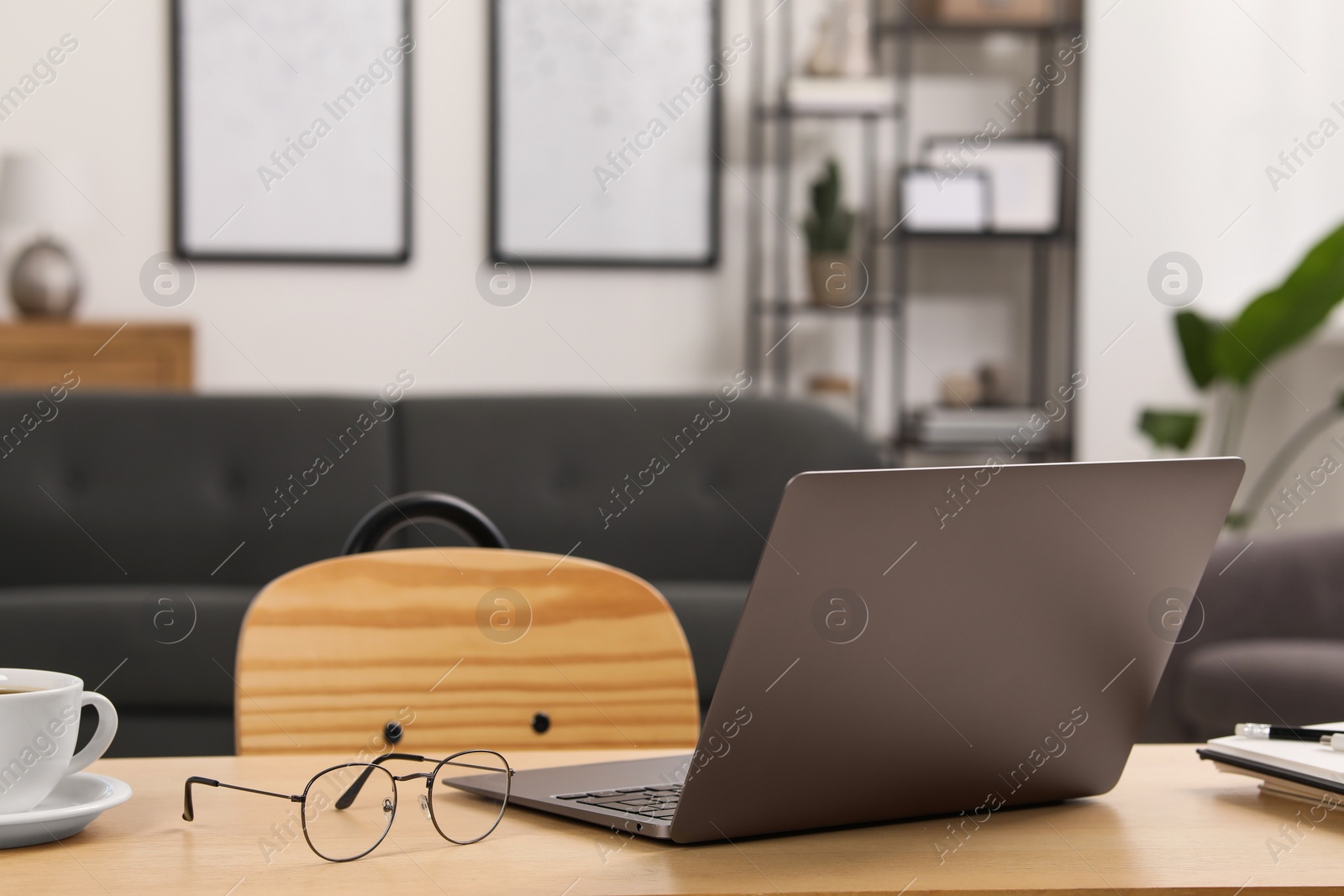 Photo of Home workspace. Laptop, glasses, cup of coffee and stationery on wooden desk in room. Space for text