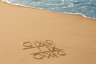 Tic tac toe game drawn on sand near sea, space for text