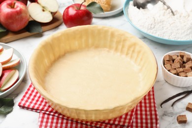 Baking dish with raw dough for apple pie and ingredients on white marble table