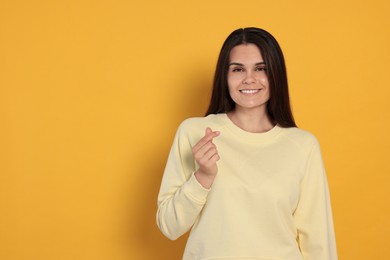 Young woman showing heart gesture on orange background, space for text