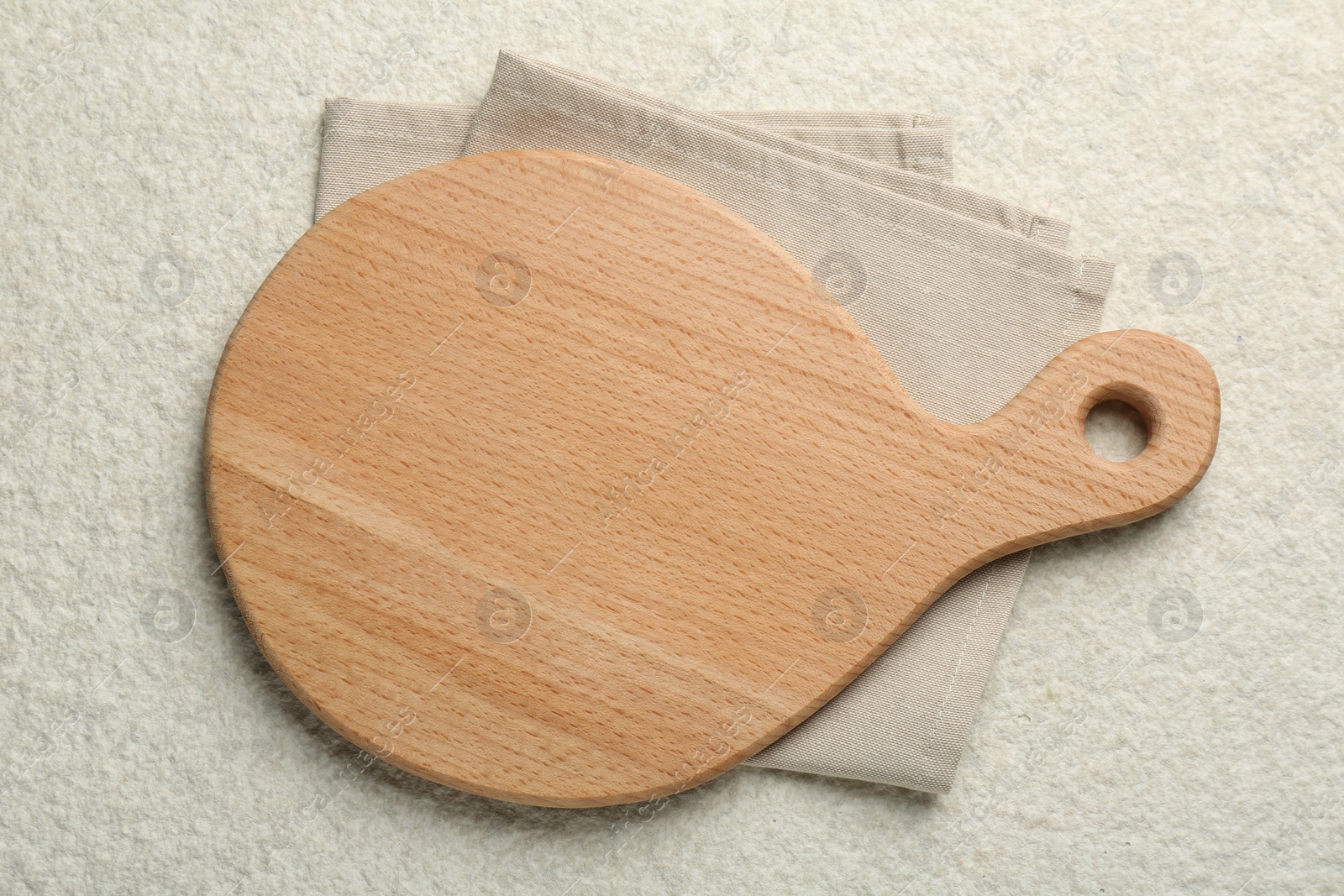 Photo of Wooden cutting board and napkin on white textured table, top view