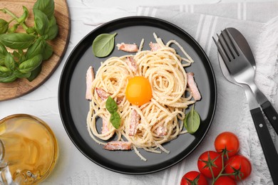 Photo of Plate of tasty pasta Carbonara with basil leaves and egg yolk on white textured table, flat lay
