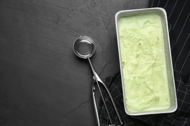 Photo of Container of sweet pistachio ice cream and scoop on black table, flat lay. Space for text