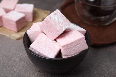Photo of Bowl of delicious sweet marshmallows with powdered sugar on brown table, closeup