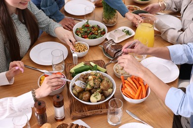 Photo of Friends eating vegetarian food at wooden table indoors, closeup