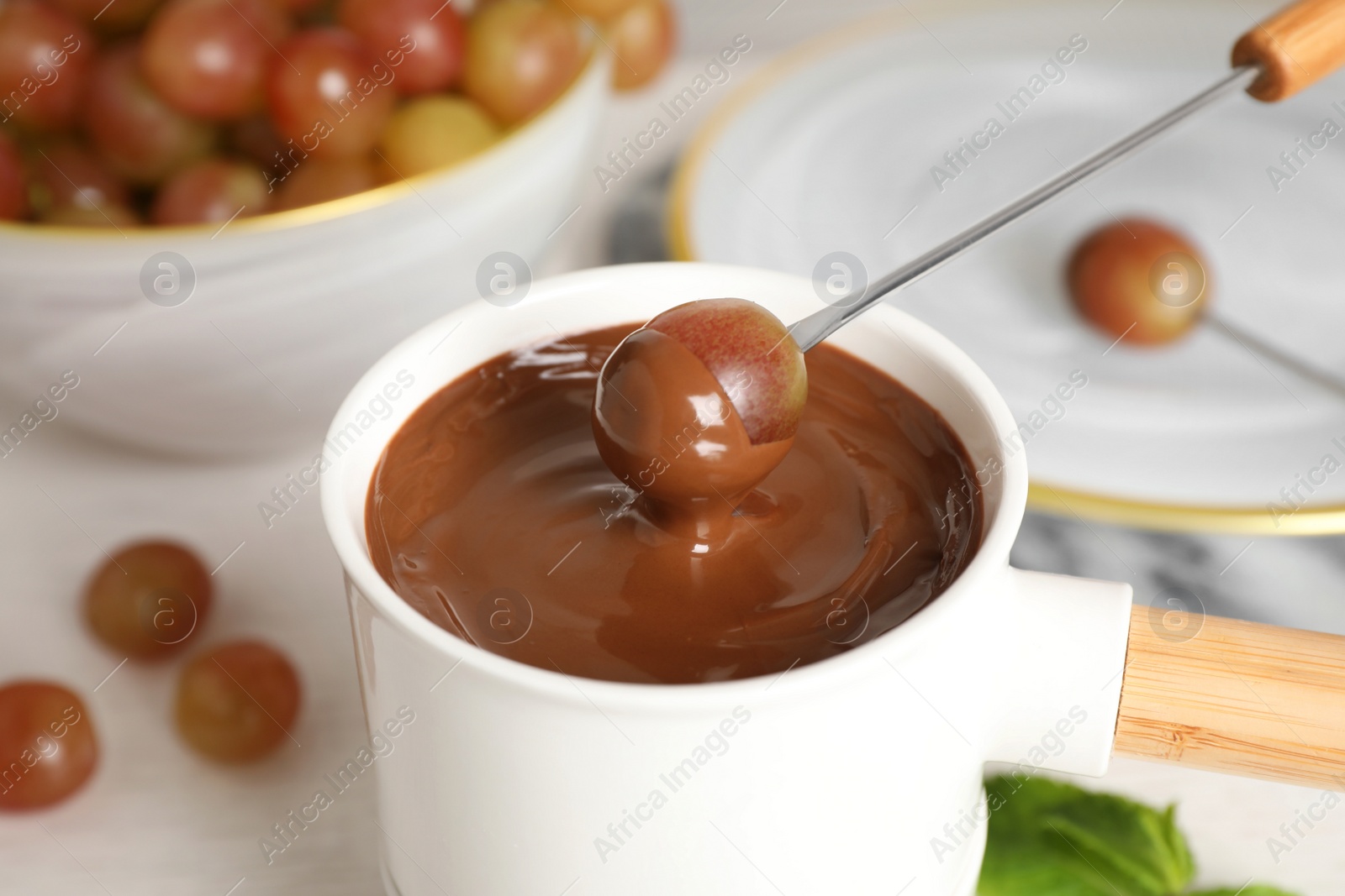 Photo of Fondue pot with chocolate and grape on white wooden table