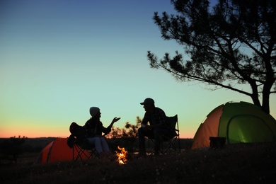 Photo of Silhouettes of couple near bonfire in evening. Camping season