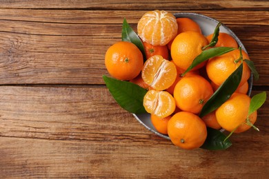 Photo of Fresh tangerines with green leaves in bowl on wooden table, top view. Space for text