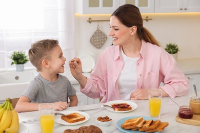 Photo of Mother and her cute little son having breakfast at table in kitchen