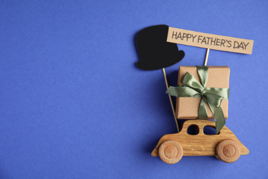 Photo of Flat lay composition with wooden car and gift box on blue background, space for text. Happy Father's day