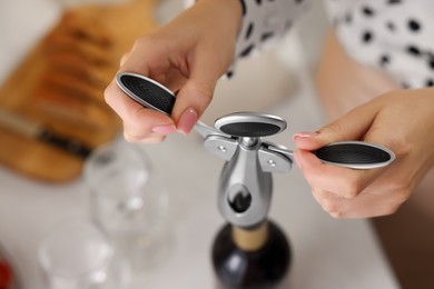 Photo of Woman opening wine bottle with corkscrew at table, above view