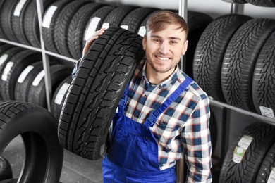 Photo of Young male mechanic with car tire in automobile service center