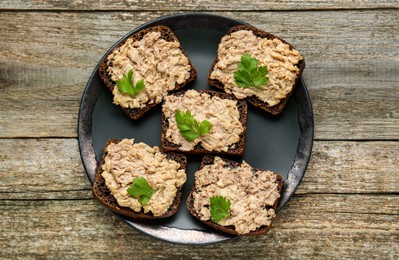 Photo of Tasty sandwiches with cod liver and parsley on wooden table, top view
