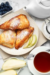 Photo of Fresh tasty puff pastry with sugar powder, pear, blueberries and aromatic tea served on white marble table, flat lay