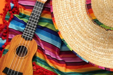 Photo of Mexican sombrero hat, guitar and colorful poncho on orange background, flat lay