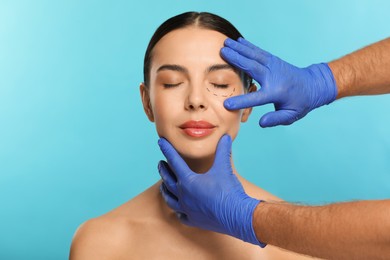 Photo of Doctor checking patient's face before cosmetic surgery operation on light blue background