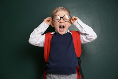 Photo of Funny little child wearing glasses near chalkboard. First time at school