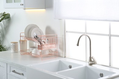 Photo of Clean dishes on drying rack in modern kitchen interior