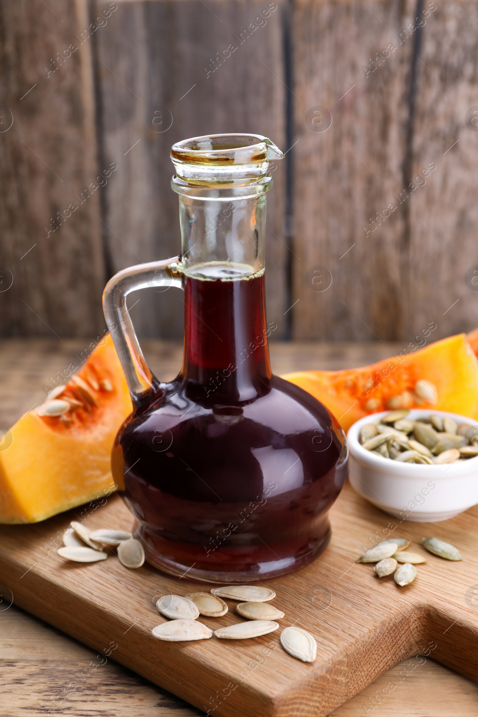 Photo of Fresh pumpkin seed oil in glass jug on wooden table