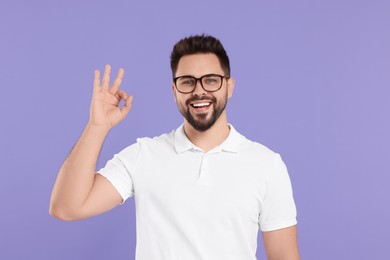 Photo of Handsome man in glasses showing OK gesture on violet background