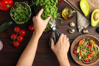 Photo of Woman cutting fresh organic microgreen at wooden table, top view