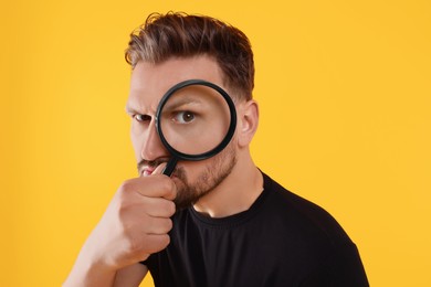 Photo of Handsome man looking through magnifier on yellow background