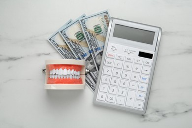 Photo of Educational dental typodont model, dollar banknotes and calculator on white table, flat lay. Expensive treatment