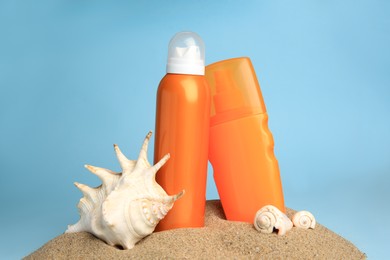 Photo of Sand with bottles of sunscreens and seashells against light blue background. Sun protection