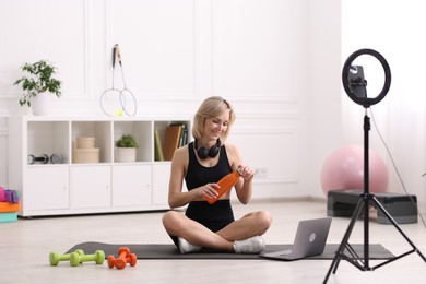 Photo of Smiling sports blogger holding bottle while streaming online fitness lesson at home