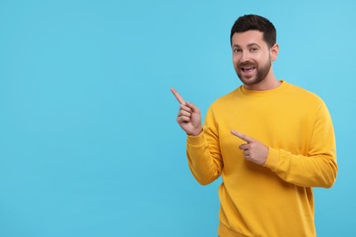 Photo of Special promotion. Handsome man pointing at something on light blue background. Space for text