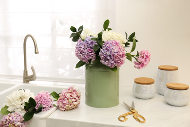 Photo of Bouquet with beautiful hydrangea flowers in can and scissors on light countertop