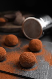 Photo of Delicious chocolate truffles powdered with cocoa on black table, closeup