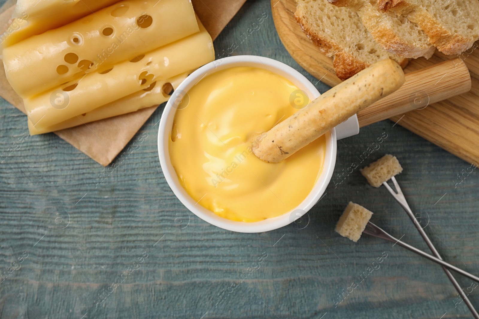 Photo of Flat lay composition with pot of tasty cheese fondue on blue wooden table