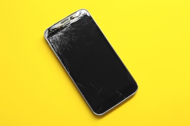 Photo of Smartphone with cracked screen on yellow background, top view. Device repair