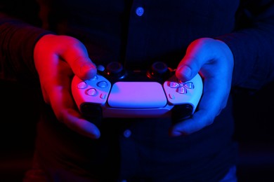 Photo of Man using wireless game controller on dark background in neon lights, closeup