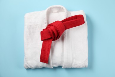 Photo of Red karate belt and white kimono on light blue background, top view