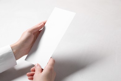 Photo of Woman holding blank card at white table, closeup. Mockup for design