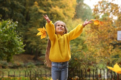 Beautiful girl playing with dry leaves in autumn park