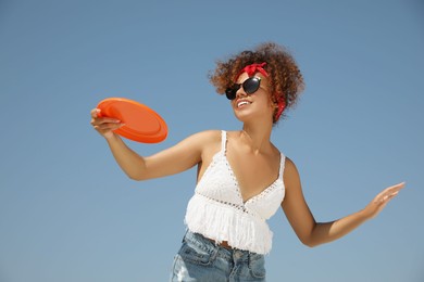 Photo of Happy African American woman throwing flying disk against blue sky on sunny day