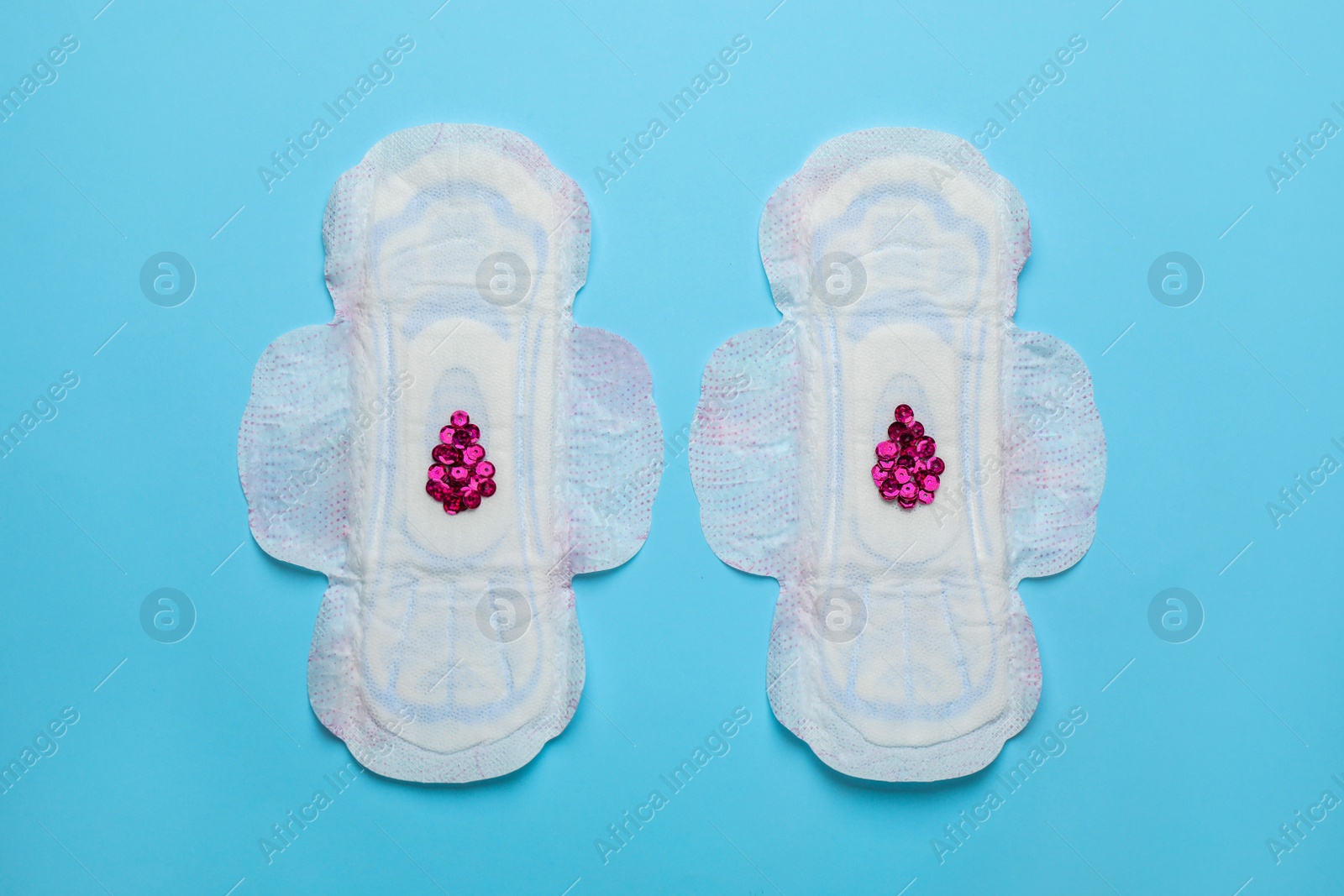 Photo of Menstrual pads with drops made of pink sequins on light blue background, flat lay