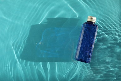 Photo of Bottle of cosmetic product in water on turquoise background, top view. Space for text