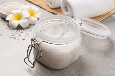Photo of Body scrub, towels and plumeria flowers on grey table, closeup