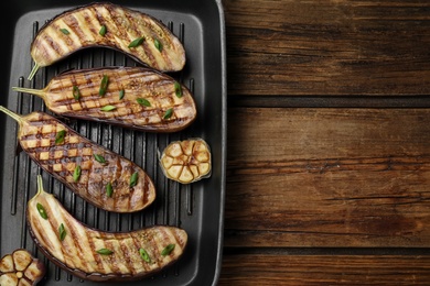 Photo of Delicious grilled eggplant halves in pan on wooden table, top view. Space for text