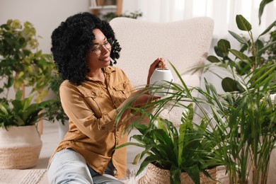 Happy woman watering beautiful houseplants at home