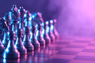Photo of Chess pieces on checkerboard in color light, selective focus. Space for text