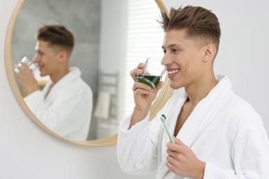 Photo of Young man using mouthwash in bathroom. Oral hygiene