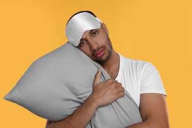 Photo of Tired man with pillow and sleep mask on orange background. Insomnia problem